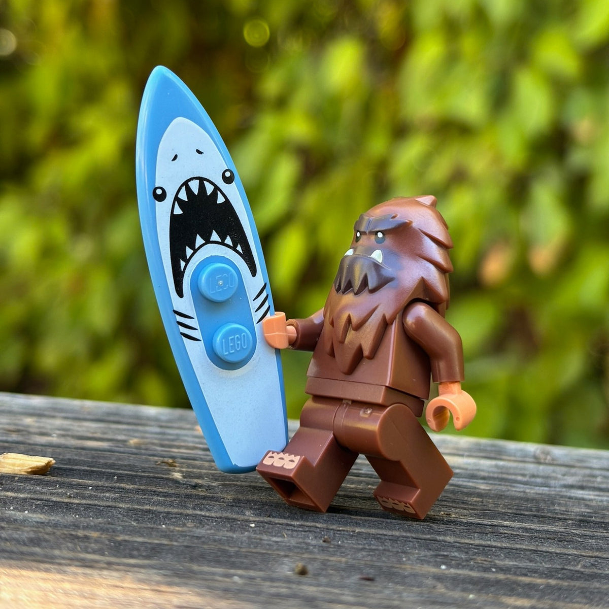 Bigfoot minifigure carrying a shark surfboard along a wooden rail